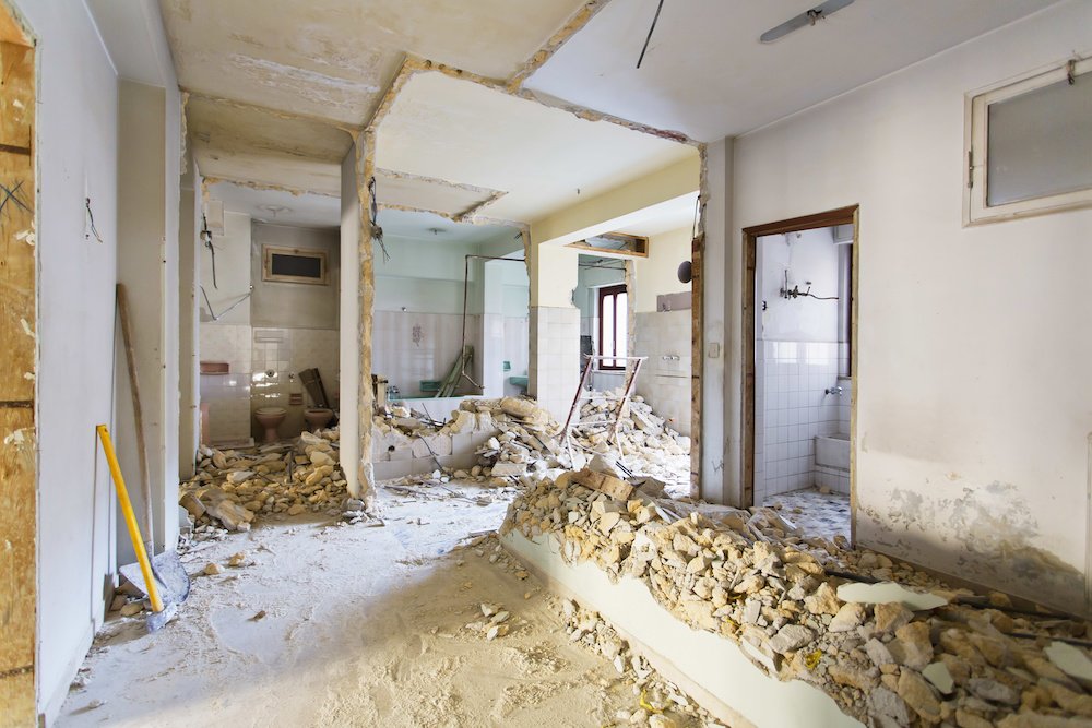 A view of the interior of a property where several walls have been taken down for renovation. The bricks and rubble sit messily on the floor.