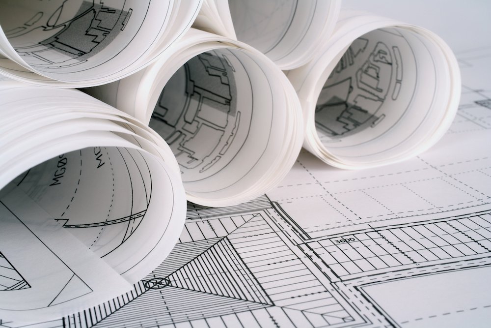 Rolled up sheets of architectural plans sit on a desk where a blueprint of a home is spread out.