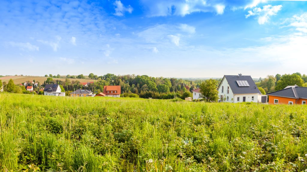 A handful of newbuild houses sit in the distance behind a green field
